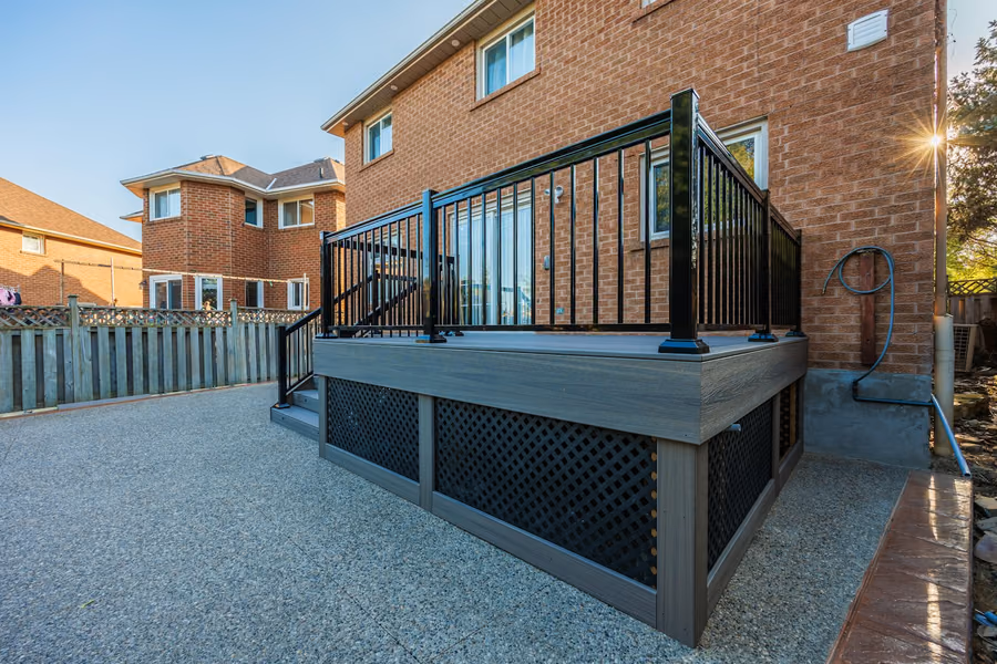 Elevated deck with gray composite boards, black aluminum picket guard, lattice skirting and a short stair run down to a concrete patio