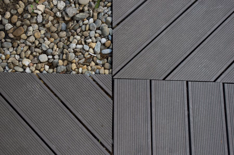 Grooved gray composite deck boards laid at a diagonal, meeting a border board, with river-rock gravel visible alongside
